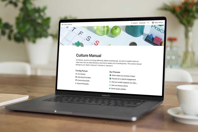 Photo of a laptop on a desk. On the screen is a document with the title “Culture Manual” followed by a list of chapters.